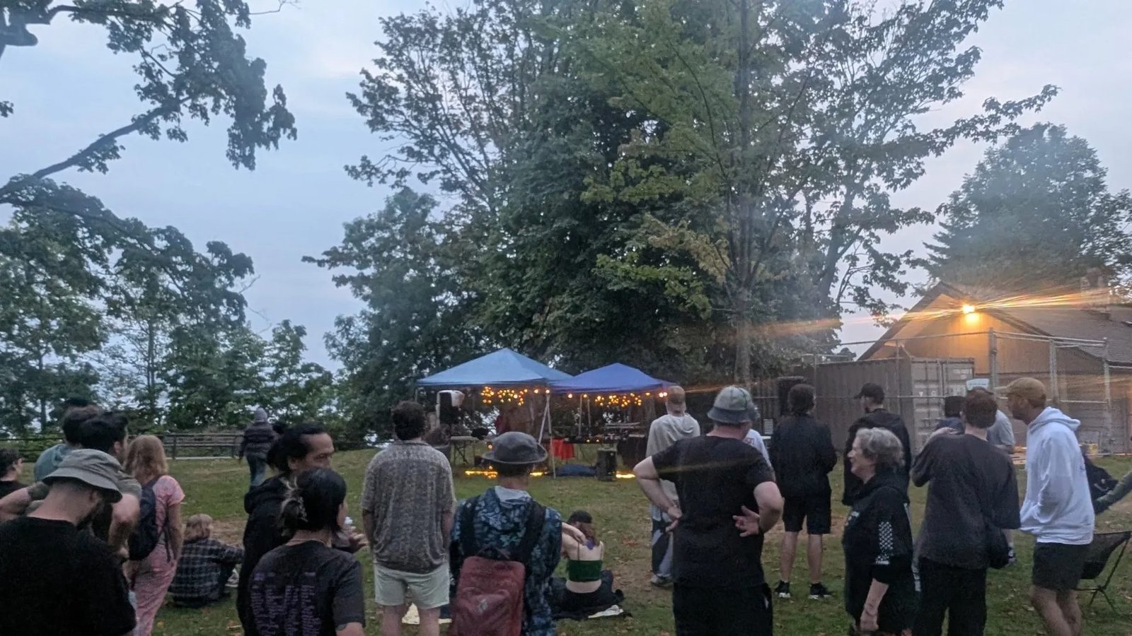 A crowd gathers on the grass at Hadden Park facing an outdoor canopy performance area at dusk.