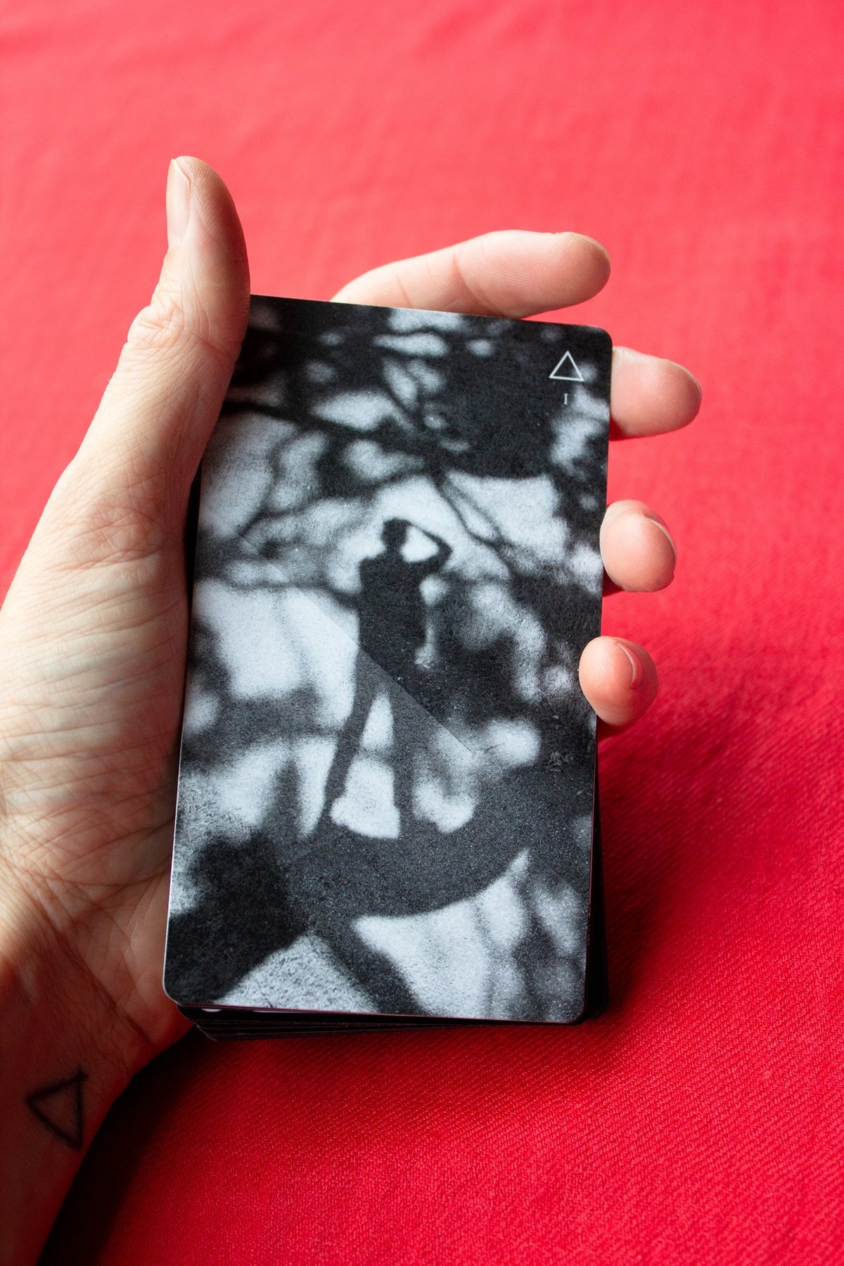 A hand holds a black-and-white photographic Tarot card from Book of Light against a red background.