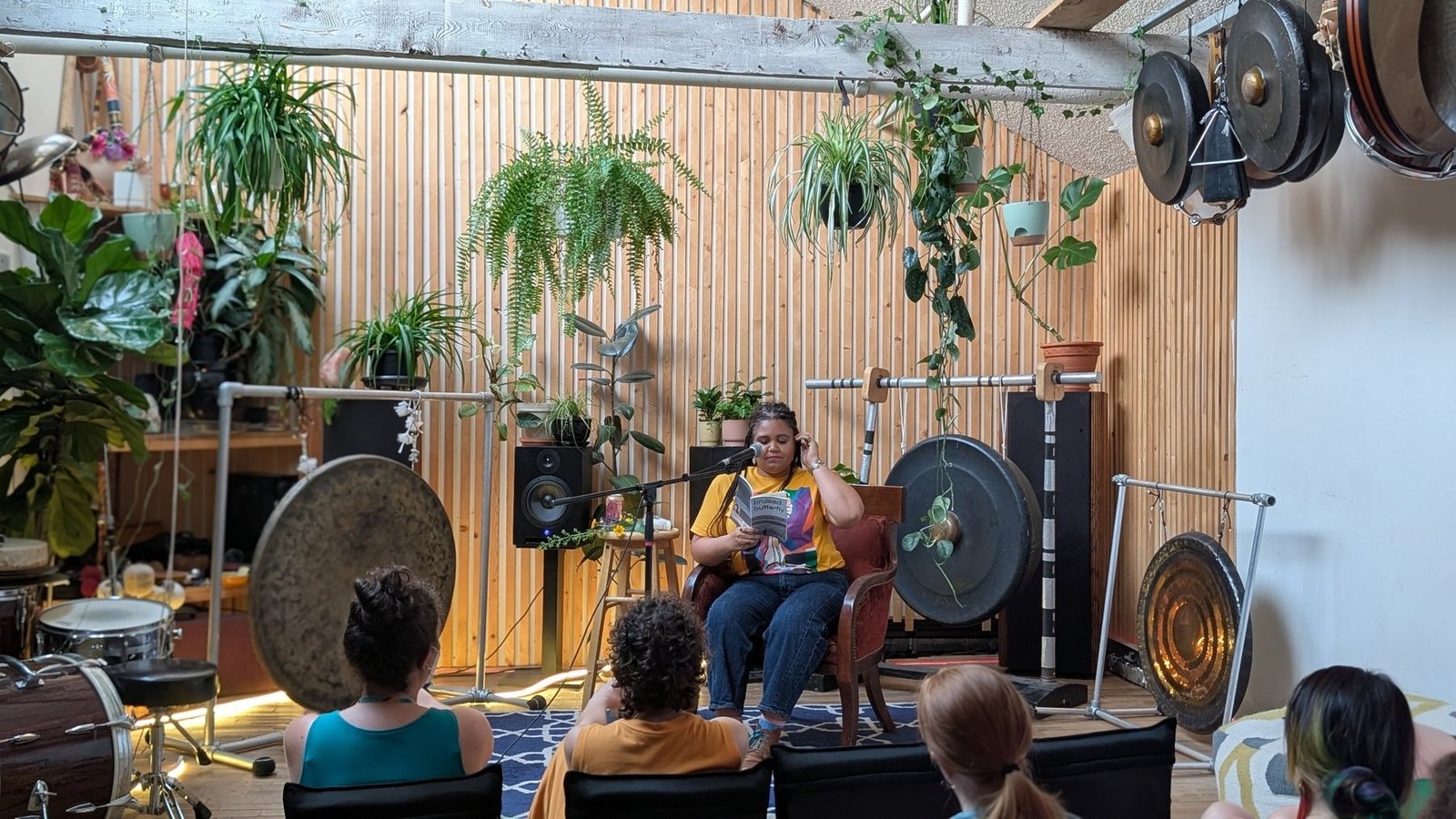 The author seated with a book and microphone during the live reading in the Gong Library.