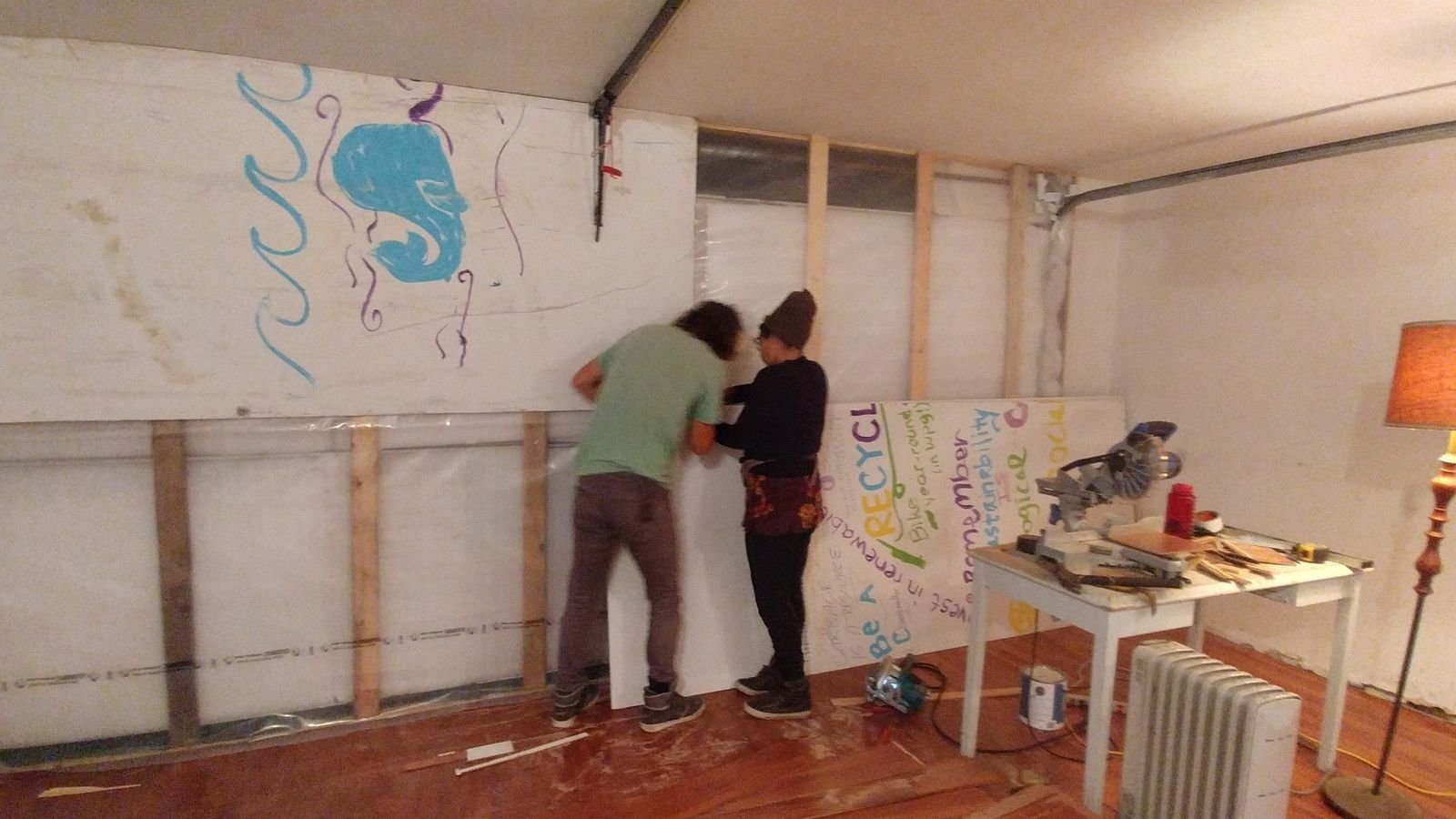Two people install wall panels inside the garage during the CLOUD Studio conversion.