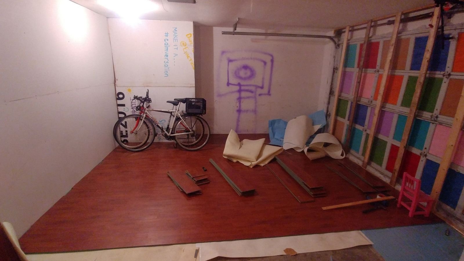 Reclaimed wood flooring is being installed across the garage floor while wall and insulation work continues.