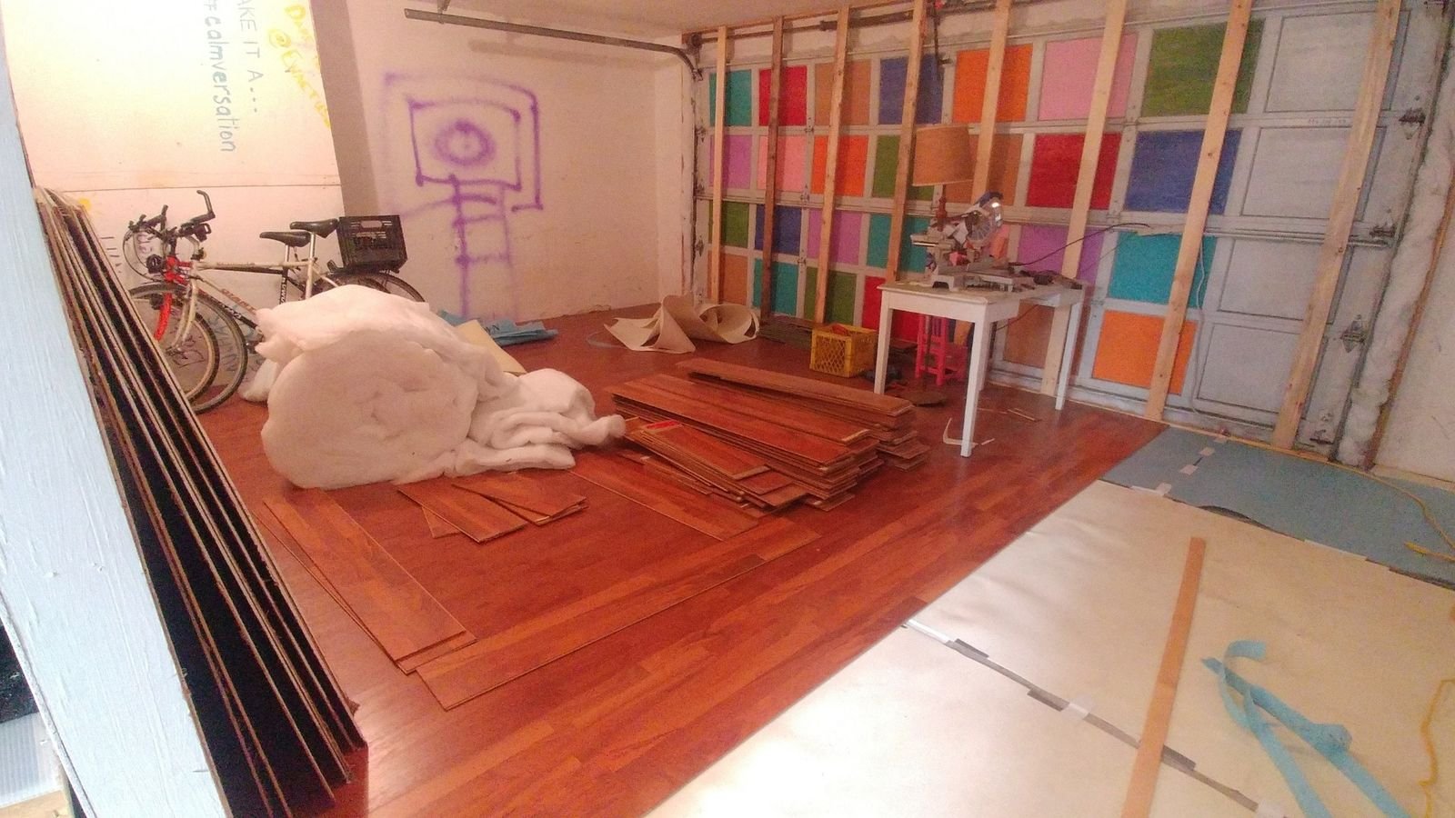 Stacks of reclaimed flooring, insulation, tools, and a partially completed studio floor during construction.