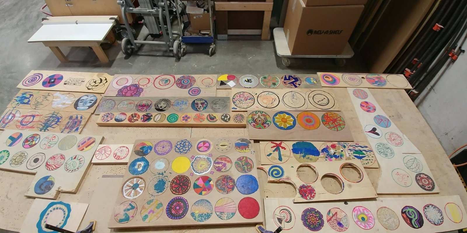 Dozens of participant-made circular glyphs painted on reclaimed wooden panels and arranged together.