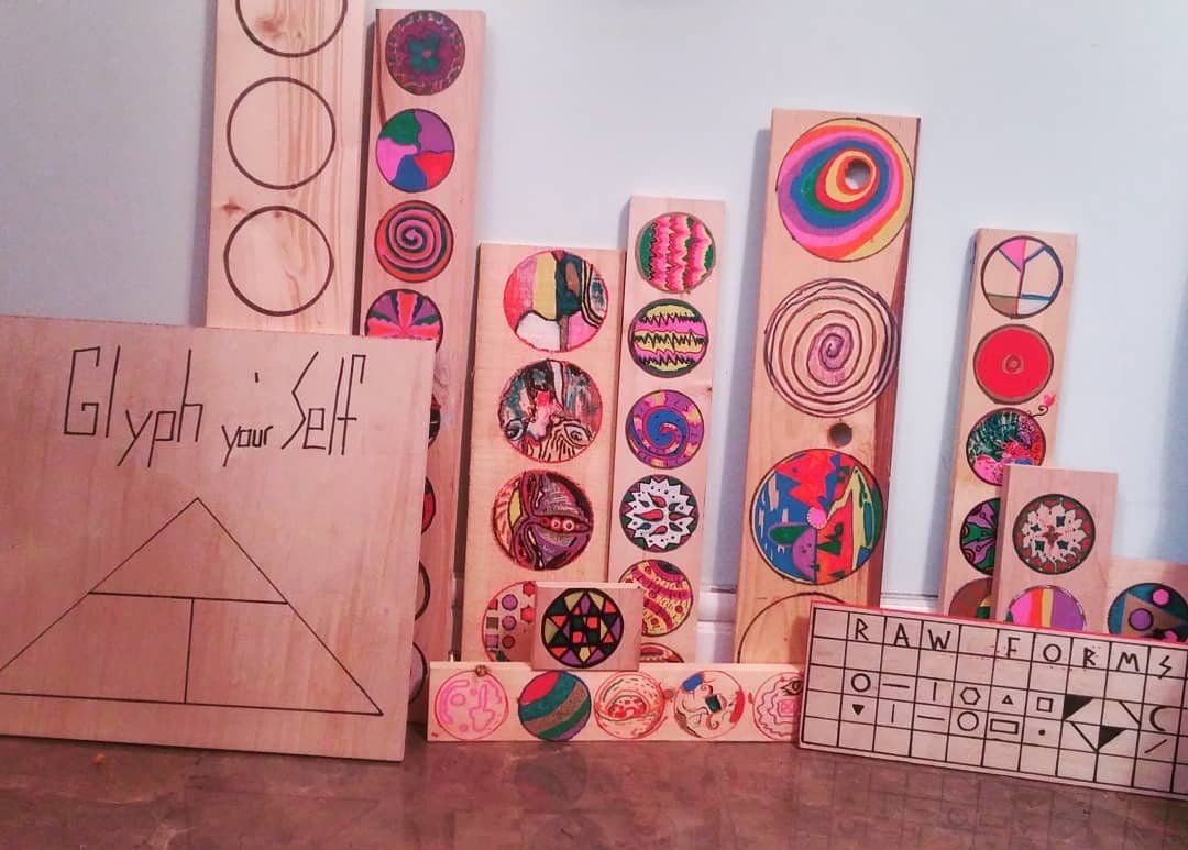 Painted wooden strips bearing colorful circular glyphs displayed with the GLYPH yo Self project sign.