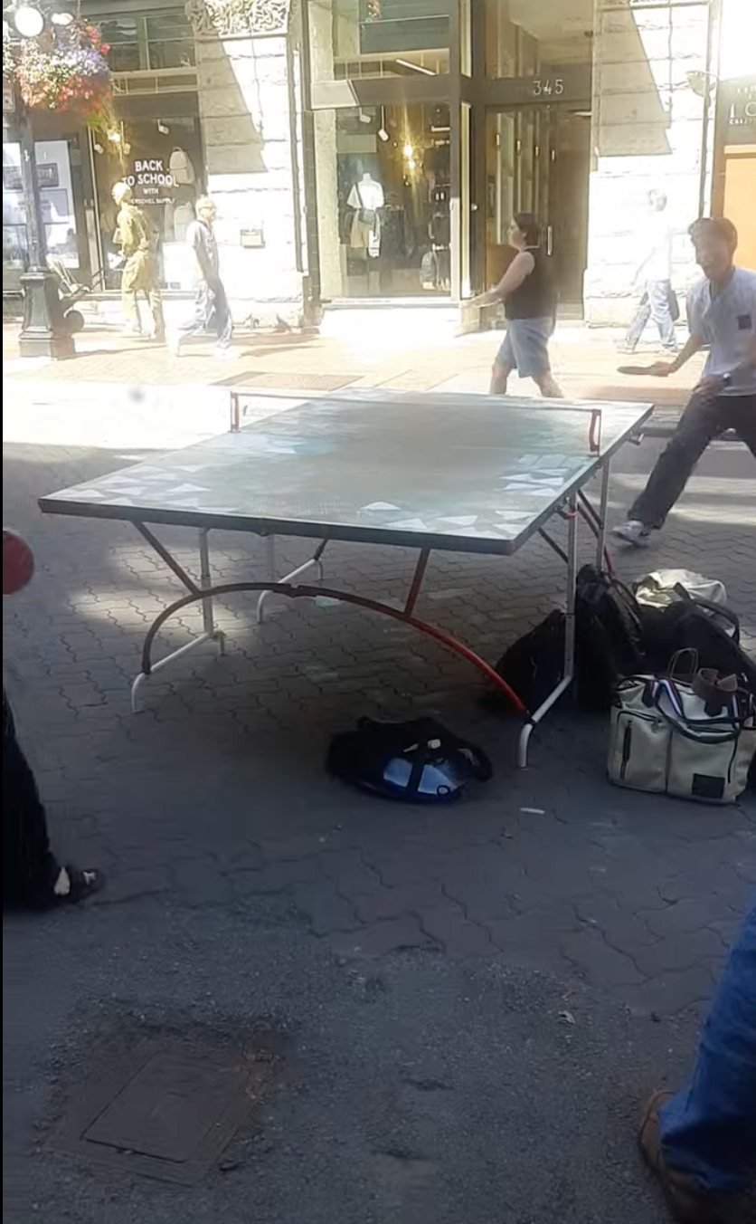 The Sonic Ping-Pong table is activated outdoors on a public sidewalk with passersby nearby.