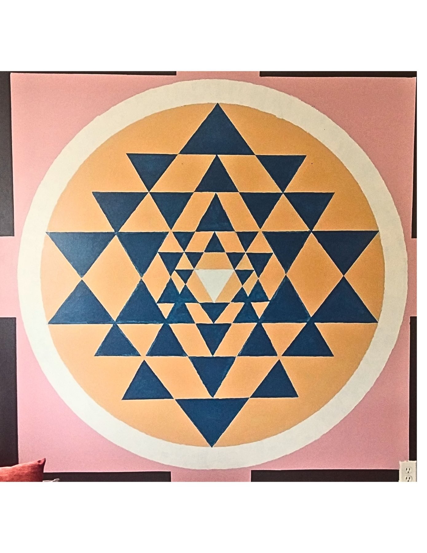 A large Sri Yantra mural painted on an interior wall, featuring dark blue triangles inside a golden circle on a pink and black background.
