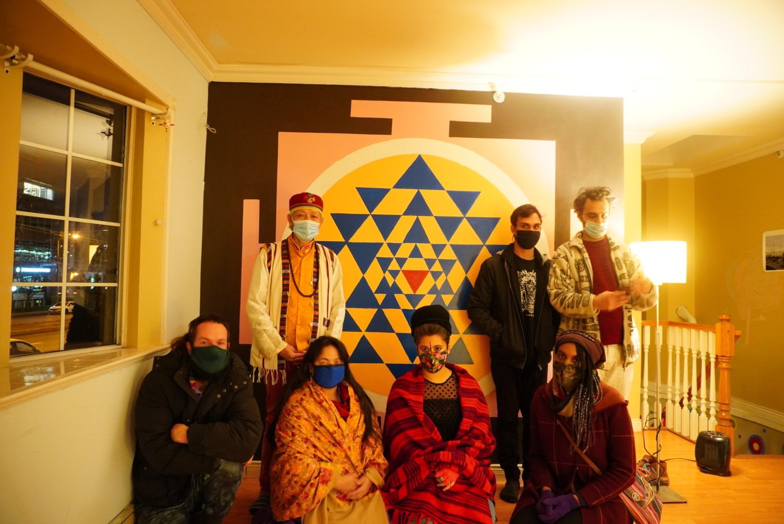 A group of participants pose indoors in front of the completed Sri Yantra mural.