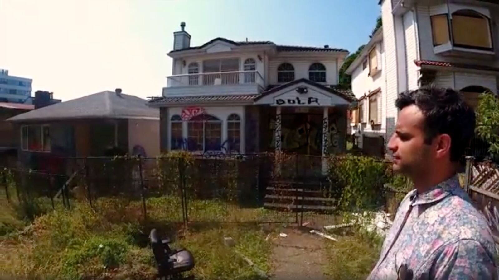 Front exterior of the boarded Wheel of Time Gallery house as Raj Gill stands in the yard