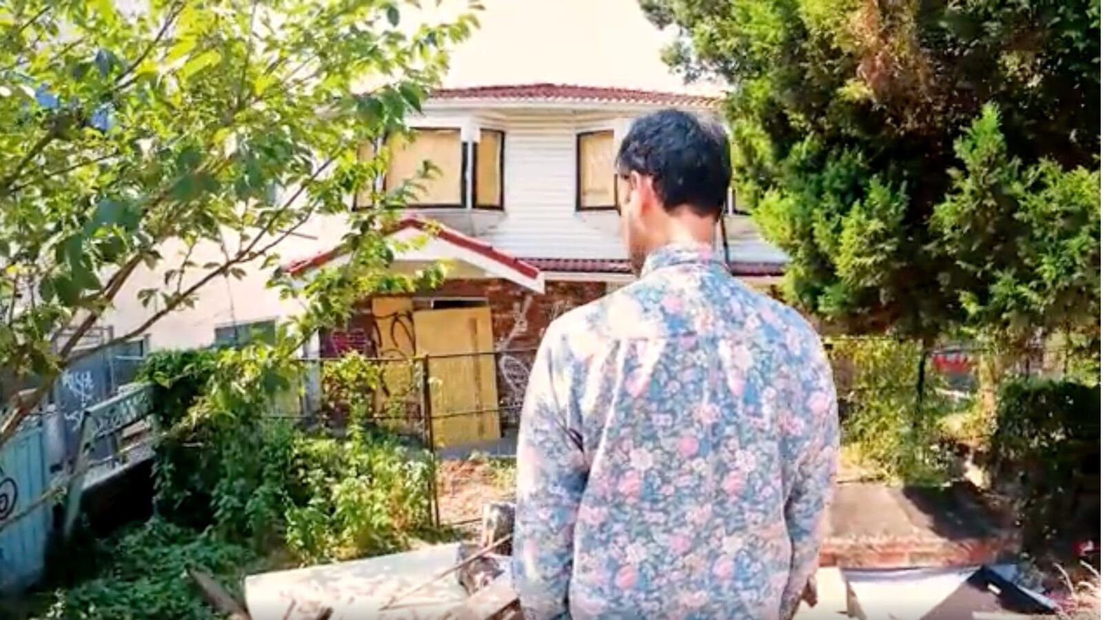 Raj Gill facing the boarded rear exterior of the house amid an overgrown garden