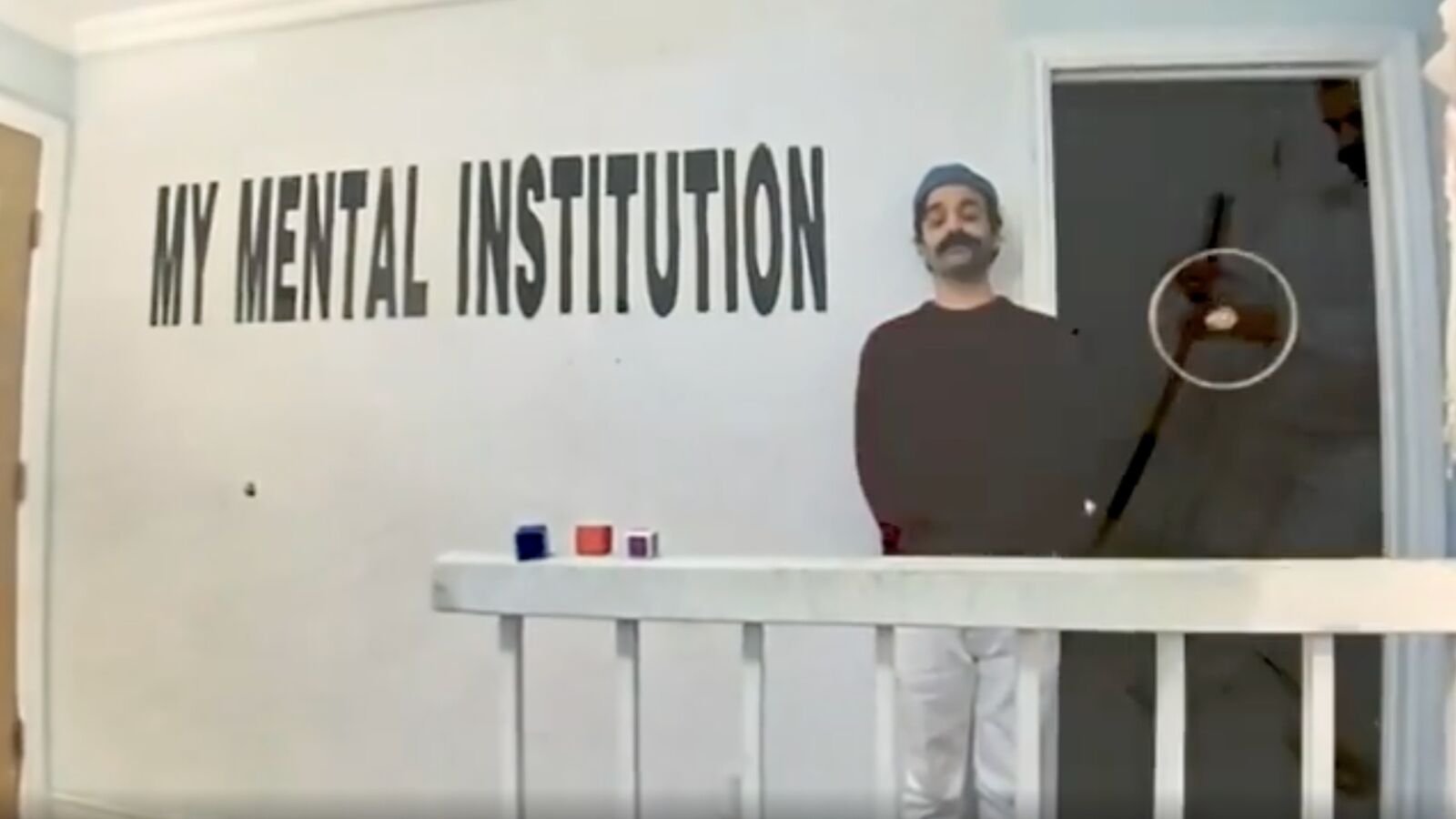 Raj Gill standing beside the My Mental Institution title wall at the entrance to the white room