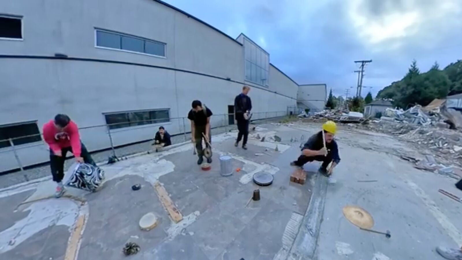 Four performers making sound with percussion and found materials on the cleared demolition site