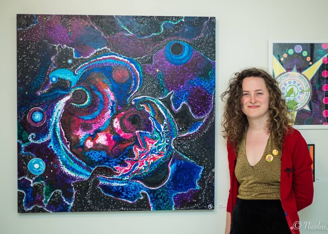 An artist standing beside a large-scale cosmic painting