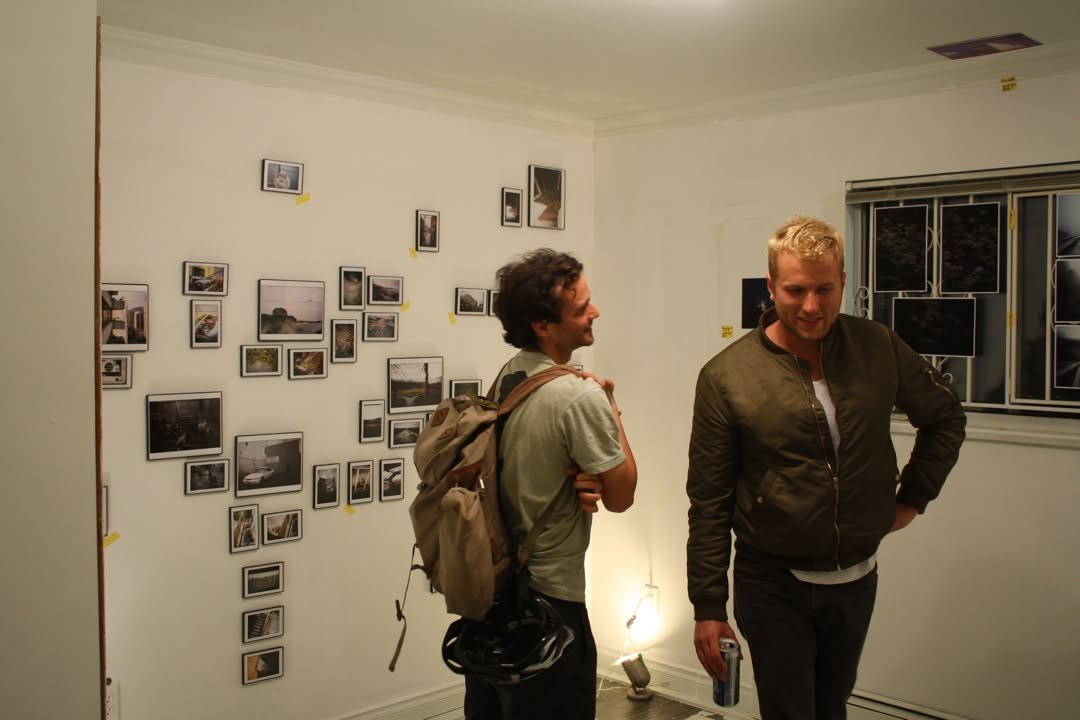 Two visitors looking at a wall of small framed photographs