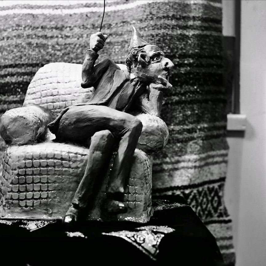 A ceramic sculpture of a pointed-hat figure reclining in an armchair
