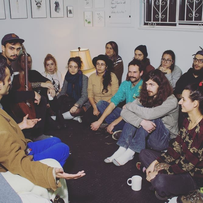 A group of people sitting in a close circle on the floor of a small room