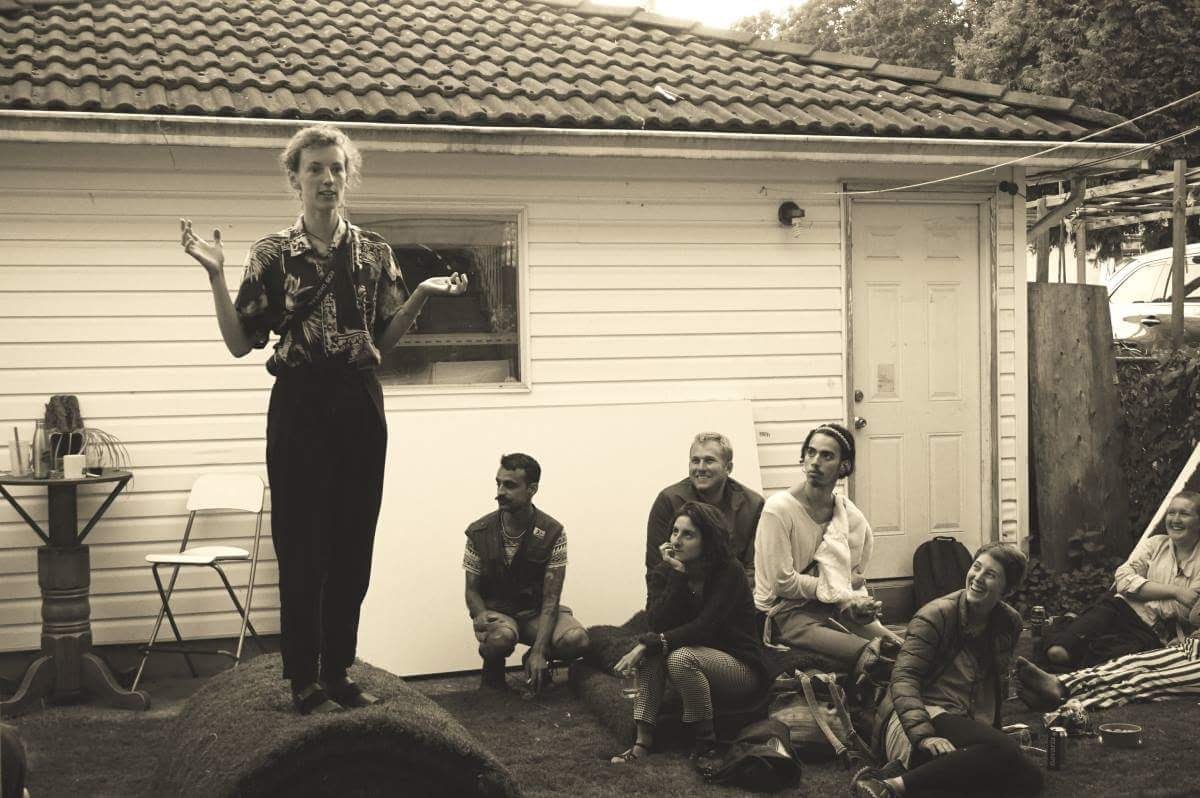 A person standing and speaking animatedly in the backyard beside the garage